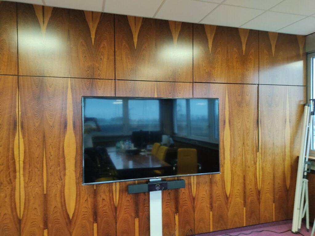 Écran mural intégré sur panneau bois dans une salle de réunion design.