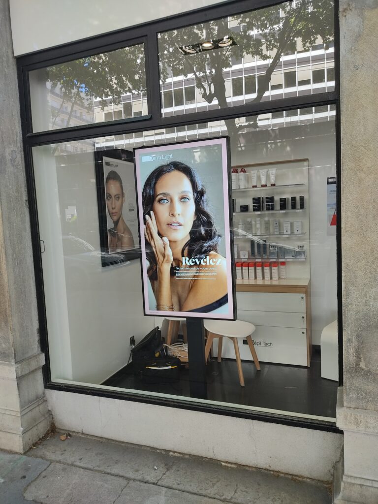 Écran vitrine diffusant une campagne beauté dans un magasin de cosmétique.