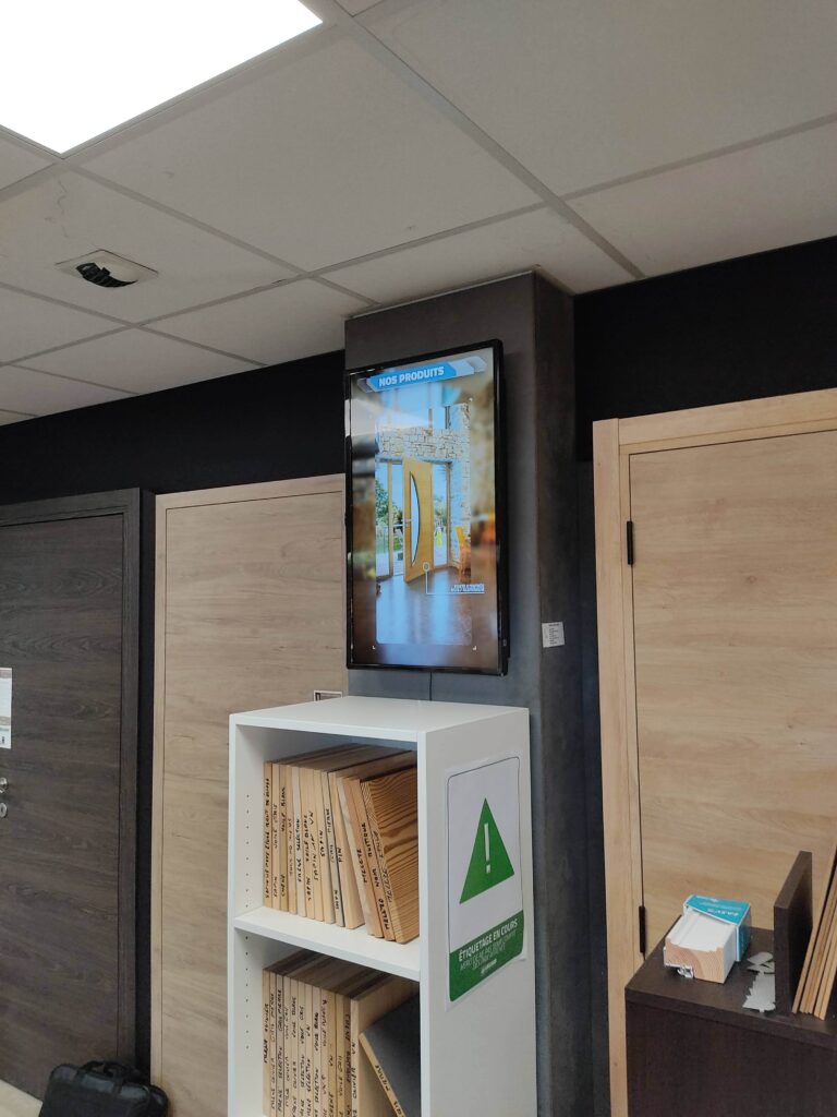 Écran mural diffusant un catalogue produits dans un showroom de menuiserie.