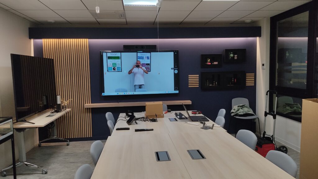 Salle de réunion d’entreprise équipée d’un écran mural et d’un système de visioconférence opérationnel.